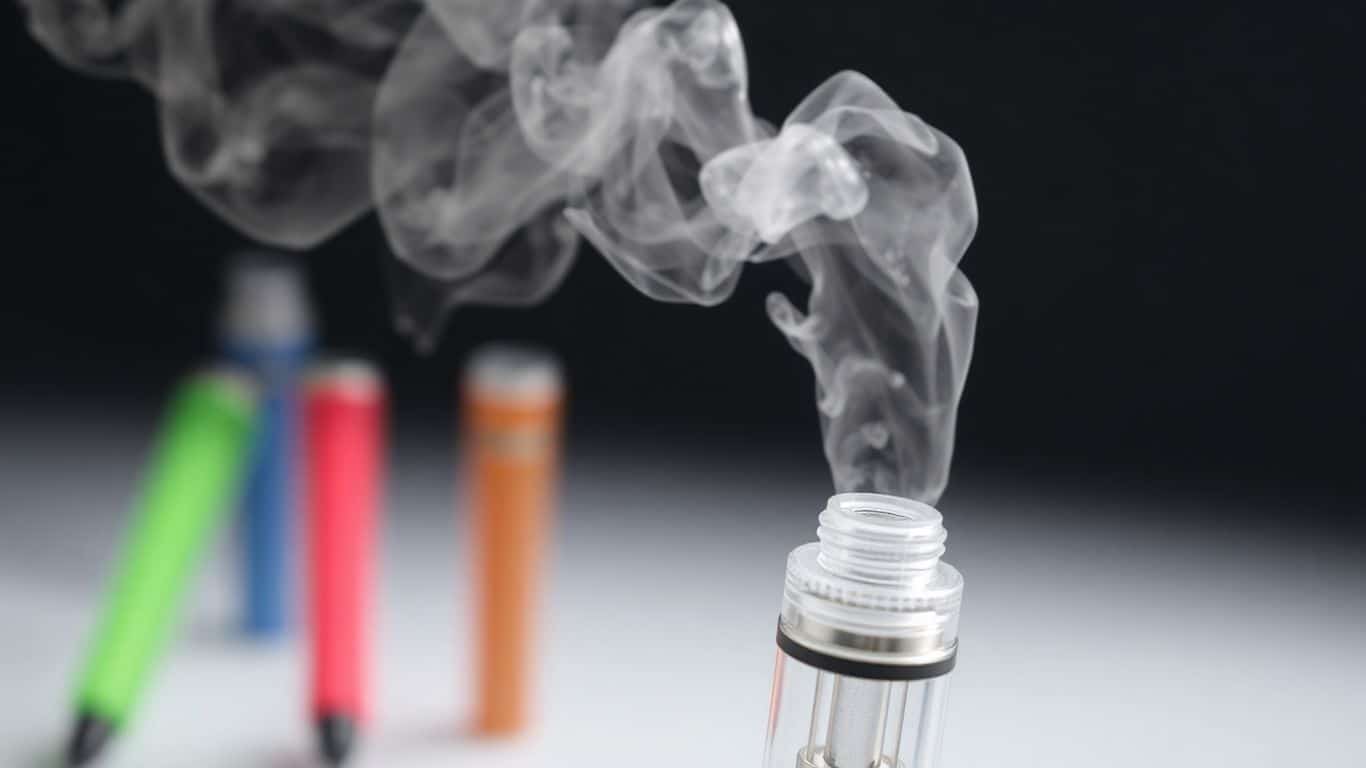 Vape pen with vapor, colorful vapes in background.